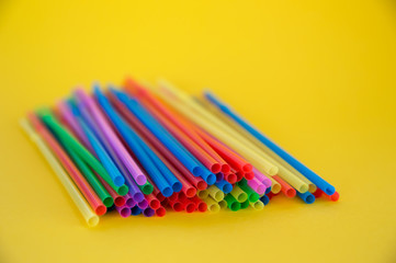 Multicolored plastic tubules for a cocktail in a glass on a yellow background. Polymers in everyday life.