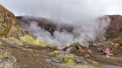 Tourists are dwarfed by the sulphurous clouds and steam that rises from the boiling lake in the vent of the crater of the active volcano - White Island, New Zealand.