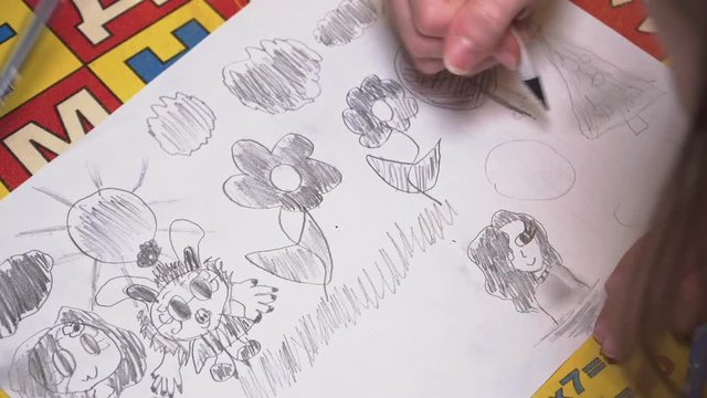 Girls draws funny picture with a bunny, flowers and clouds on the album sheet close up