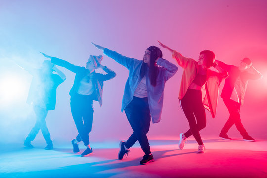 Young modern dancing group of six adult young people practice dancing on colorful background. Fashionably dressed youngsters moving over blurred disco club color lights