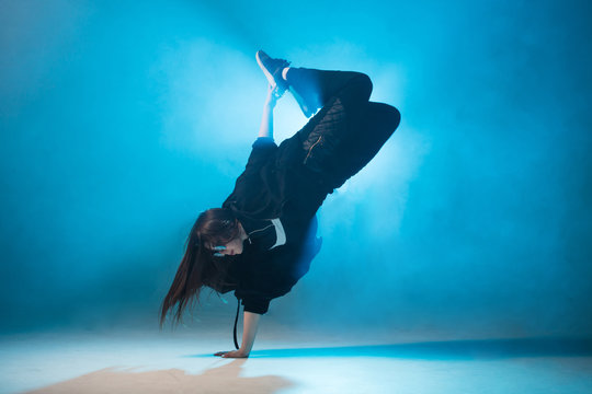 Young hip-hop female dancer performing solo on the stage in blue neon lights with flash light in the middle