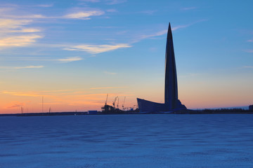 The Lahta center skyscraper buidling on the shore of Finish bay covered with ice and snow near Petersburg city in the mouth of Neva river in the rays of setting sun