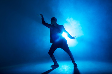Obraz na płótnie Canvas silhouette of single male break dancer isolated on blue neon background with light flare in middle