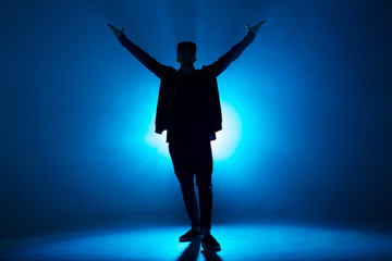 Full-size of silhouette of male break dancer performing on blue neon stage his expressive dance, Dark blue background with light flare on background - obrazy, fototapety, plakaty