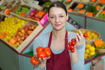 female greengrocer holding two different varieties of tomatoes