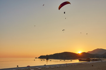Seascape with silhouettes of the mountains and coast of sea at sunset. Paraglider flying over the beach of Oludeniz in golden sunlight.