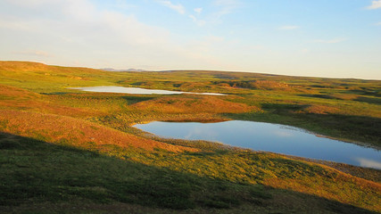 Summer photograph of the landscape of the tundra. The photo shows the sky with clouds, lakes and mountains. Photo with a sloping horizon.