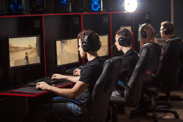 group of concentrated guys in headphones enjoying online video game on powerful computers of gaming centre, rear view. © alfa27