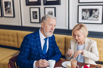 serious elegant man drinking coffee while his colleague eating a cake. close up photo. pleasant...