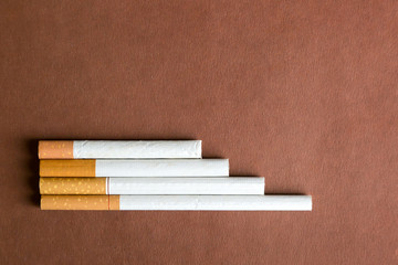 Cigarettes of different lengths on a dark background. Cigarettes of tobacco with a filter of different sizes in length on a brown background.