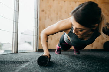Fototapeta na wymiar Gym woman doing push-up exercise with dumbbell