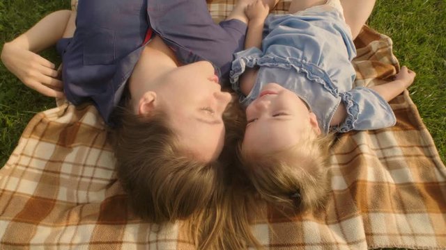 Close-up of baby girl with mother lying on green grass in the summer light in park and laughing and hugging. Slowmotion. Baby have fun. Happy family concept.
