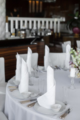 closeup white napkins stand in  white plates on served table in the restaurant. clean white dishes layout on a white tablecloth