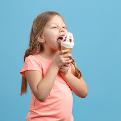 Cute little girl eats ice cream and laughs in studio over blue background