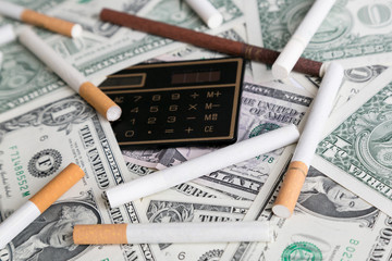 Calculator and cigarettes lie on a pile of money. Rising prices for tobacco cigarettes, concept. High cigarette prices count smoking costs.