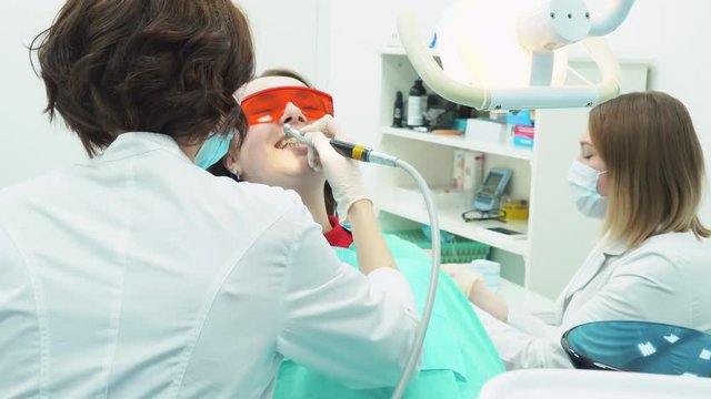 Close-up of medical dentist team in dental office making a teeth cleaning to female young patient. Dental care.