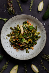Baked or stewed vegetables in a plate and fruits and herbs on a black background, top view, close-up