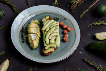 Close-up of avocado slices on rye bread and hazelnuts in a plate on a black background