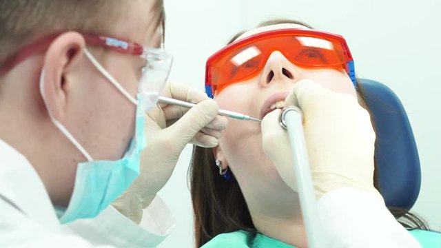 Close-up of young dentist using drill and mirror for teeth treating of female young patient at the dental office. Dental care.
