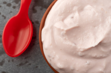 Small bowl of red raspberry yogurt with a spoon to the side on a gray background top close view