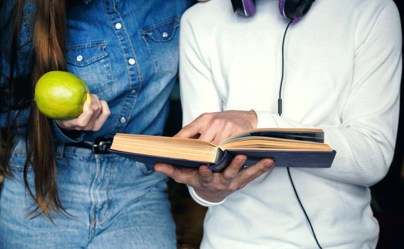 Croped view of two studens holding apple and book while preparing to the lesson
