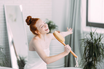 Emotional red-haired playful woman with bodybrush cheering and laughing as she singing song like a...