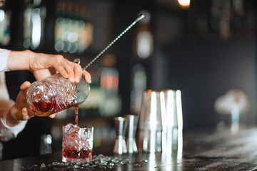 Cropped shot of bartender pouring ruby cocktail into crystal glass. Bar, Restaurant Beverage and Service concept.