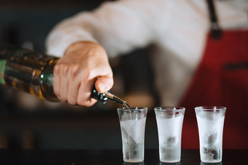 Close up photo of hands of a bartender pouring some drink from the bottle into shot frozen glasses...