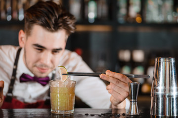 Bartender finishes decoration of his cocktail with ice cubes and lime slice using tweezers.