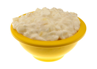 Side view of a small yellow bowl filled with pineapple cottage cheese on a white background