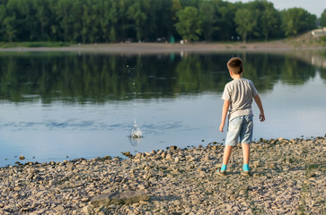 Fototapeta na wymiar a child, a teenager, on a stony shore throws stones into the river, lake