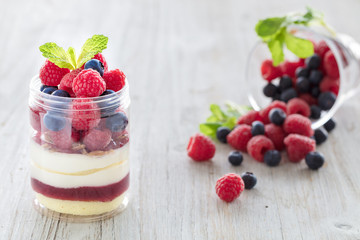 Raspberry and blueberry dessert, cheesecake, trifle, mouse in a glass jar on a light wooden background