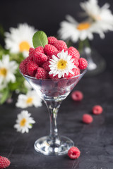 Fresh Deluxe Raspberries in martini glass with field flowers on dark wooden background, vertical composition.
