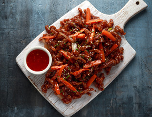 Crispy shredded beef with carrots and sweet chilli sauce on white wooden board. Chinese takeaway...