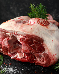 Raw lamb leg on black stone table with herbs. garlic, rosemary, chilli, salt, pepper, Bay leaf.
