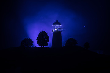 Lighthouse with light beam at night with fog. Old lighthouse standing on mountain. Table decoration. Toned background. Moonlighting.