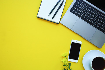 Smartfon and note, flowers, coffee laptop on yellow background. Copy space