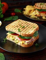 Sandwich with ham, cheese, tomatoes, spinach, corn, mayonnaise, mustard, gherkins, toasted bread and potato chips.