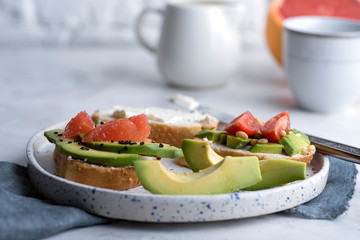 Close-up of oasts with avocado, tomatoes and cream cheese on a white plate. Breakfast or lunch concept