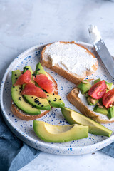 Toasts with avocado, tomatoes and cream cheese on a white plate. Breakfast or lunch concept, high angle view