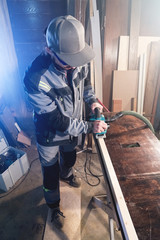 Portrait of a young carpenter working with an electrical plane in a home wood workshop. The concept of a business idea and a woodworking startup. Wide angle