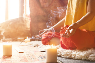 Close-up a girl surrounded by candles at home at the window meditates in the lotus position making...