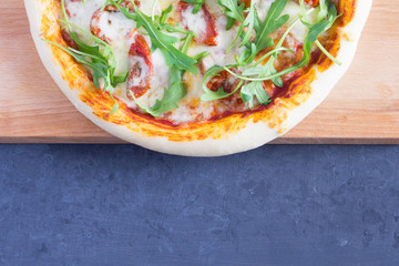 Pizza with dried tomatoes, arugula and mozzarella on a gray-blue dark background with copy space