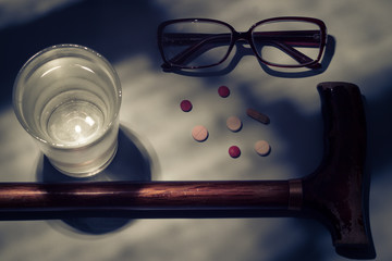 On a blue background are glass glasses, an elderly man's cane and medicines or pills.