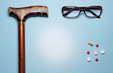 On a blue background are glass glasses, an elderly man's cane and medicines or pills.