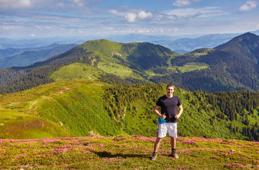 Hiker man standing near camping tent in carpathian mountains. Tourist enjoy mountain view.
