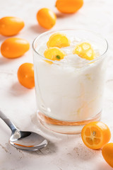 Transparent glass with white fat yogurt with kumquat slices and metal spoon on white  background. Vitamins against virus concept. Healthy food during quarantine.