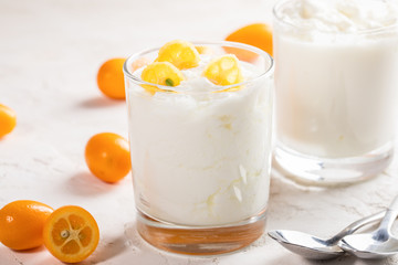 Two glasses with  yogurt with kumquat slices and two spoons on white background.