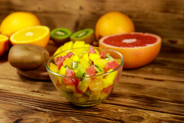 Tasty fruit salad in glass bowl and fresh fruits on the wooden table