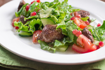 Warm salad with fried chicken liver and pomegranate seeds. Wooden background